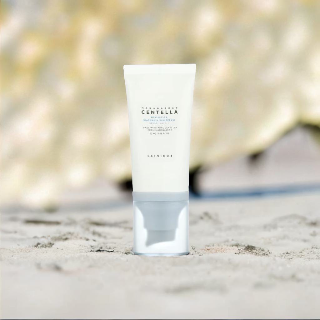 SKIN1004 Madagascar Centella Hyalu-Cica Hydrating Sun Serum SPF 50 offers hydration and UV protection on a sandy background.